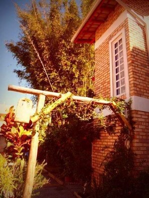 Un edificio de ladrillo con una ventana y una estructura de madera cubierta de hiedra.