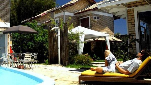 Un espace piscine avec des chaises longues, une tente et une maison en briques en arrière-plan.