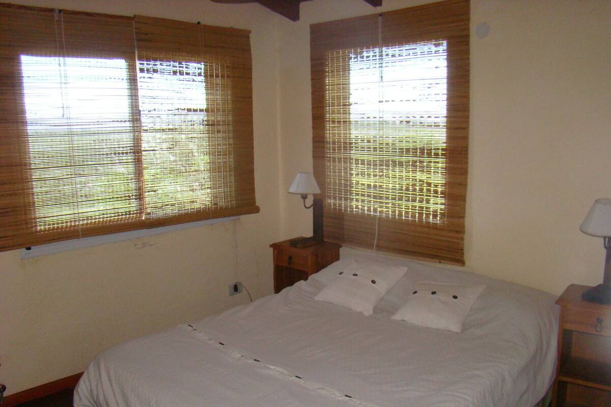 Quarto com cama, duas mesas de cabeceira, abajur e janela com persianas.