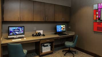 A hotel office with two computer monitors, a desk, chairs, and a printer.