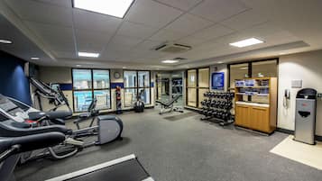 Un gimnasio con cintas de correr, bicicletas estáticas y un soporte para pesas.