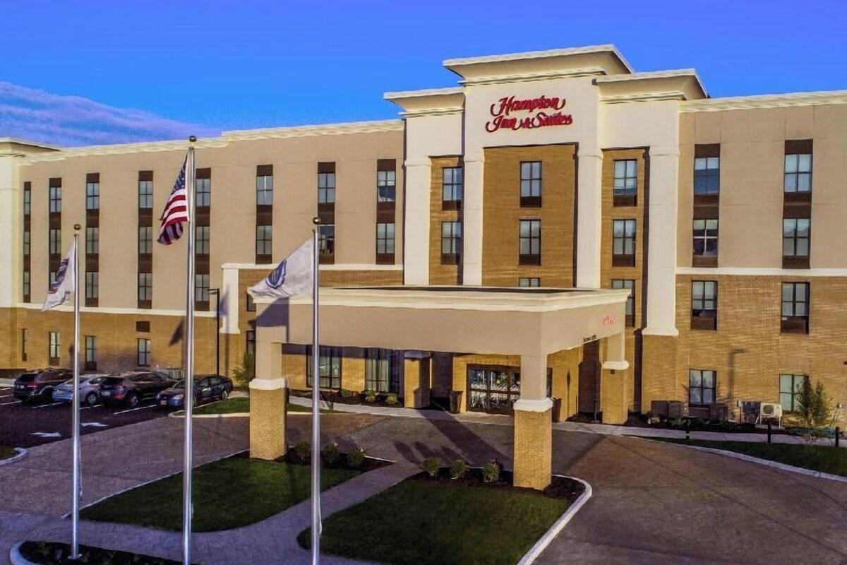Un hôtel Hampton Inn & Suites doté d’une entrée principale, de plusieurs mâts de drapeaux et d’un parking.