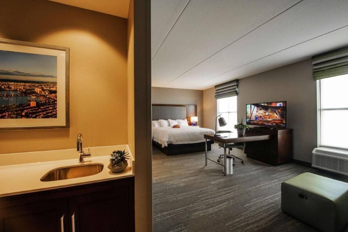 A hotel room with a bed, desk, TV, and a view of a cityscape.