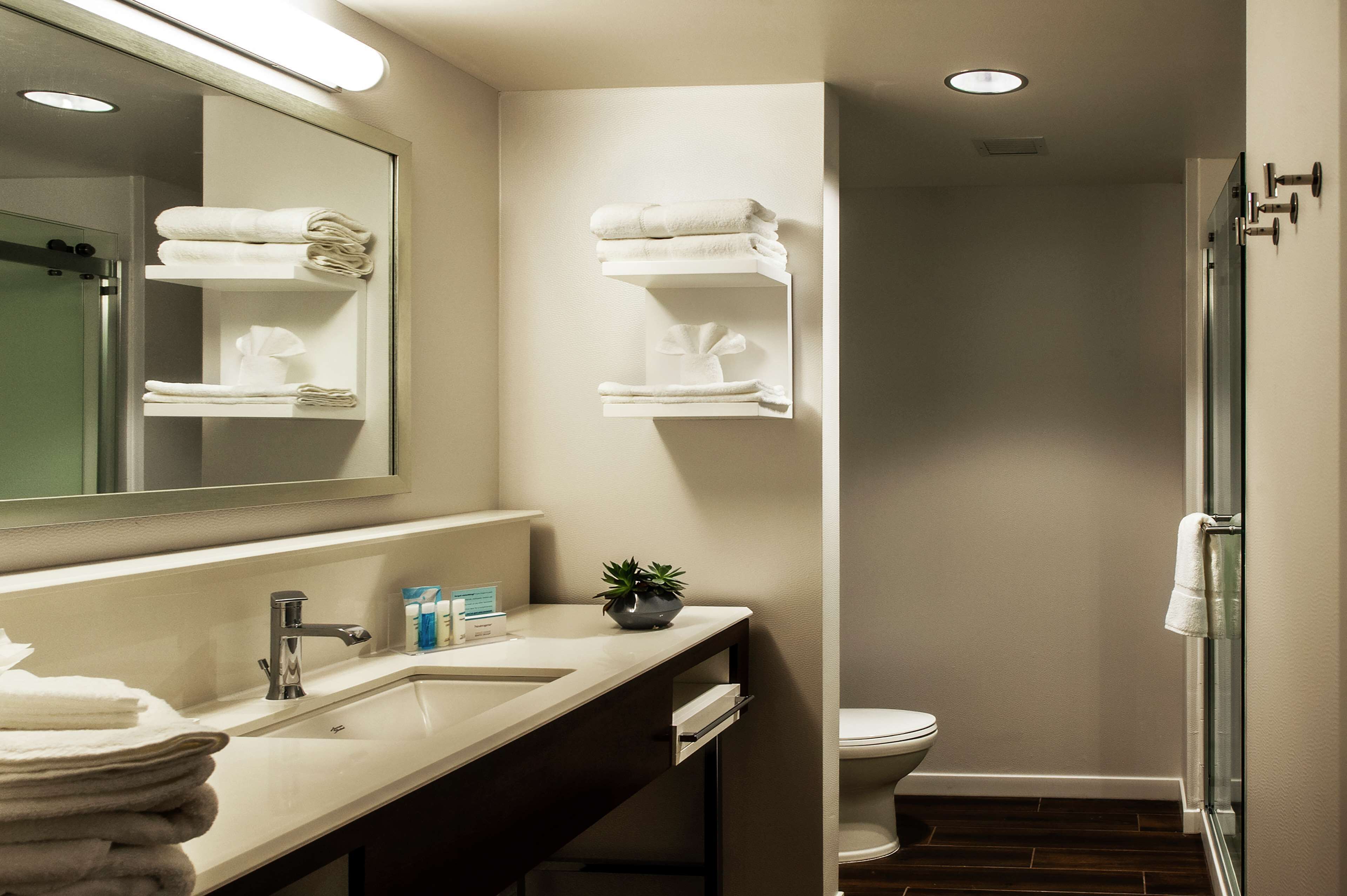 Un baño moderno con lavamanos, espejo y dos barras para toallas.