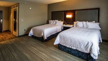Habitación de hotel con dos camas, una mesita de noche con lámpara y una puerta que da a otra habitación.