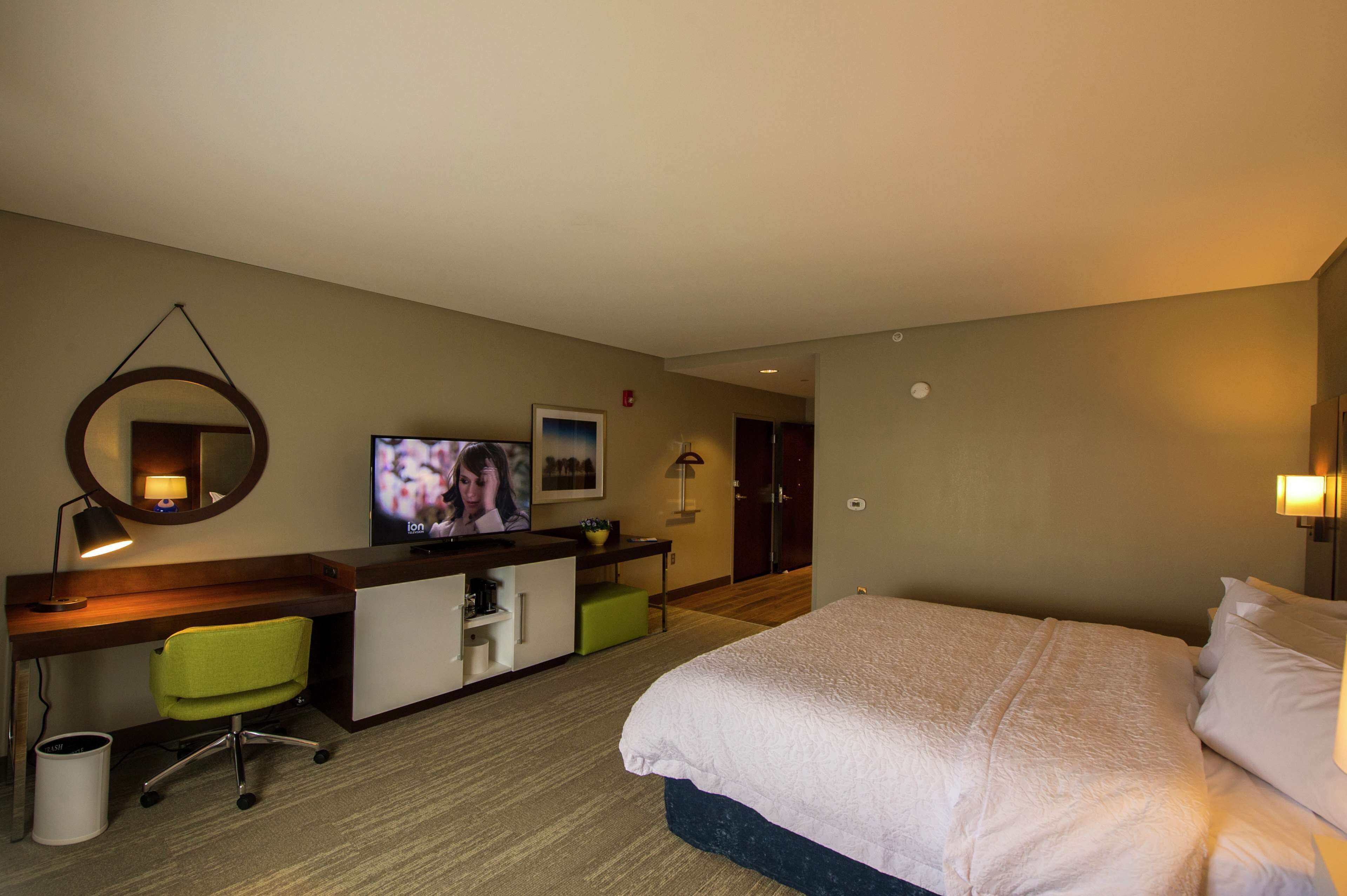 A hotel room with a bed, desk, chair, TV, and a mirror.