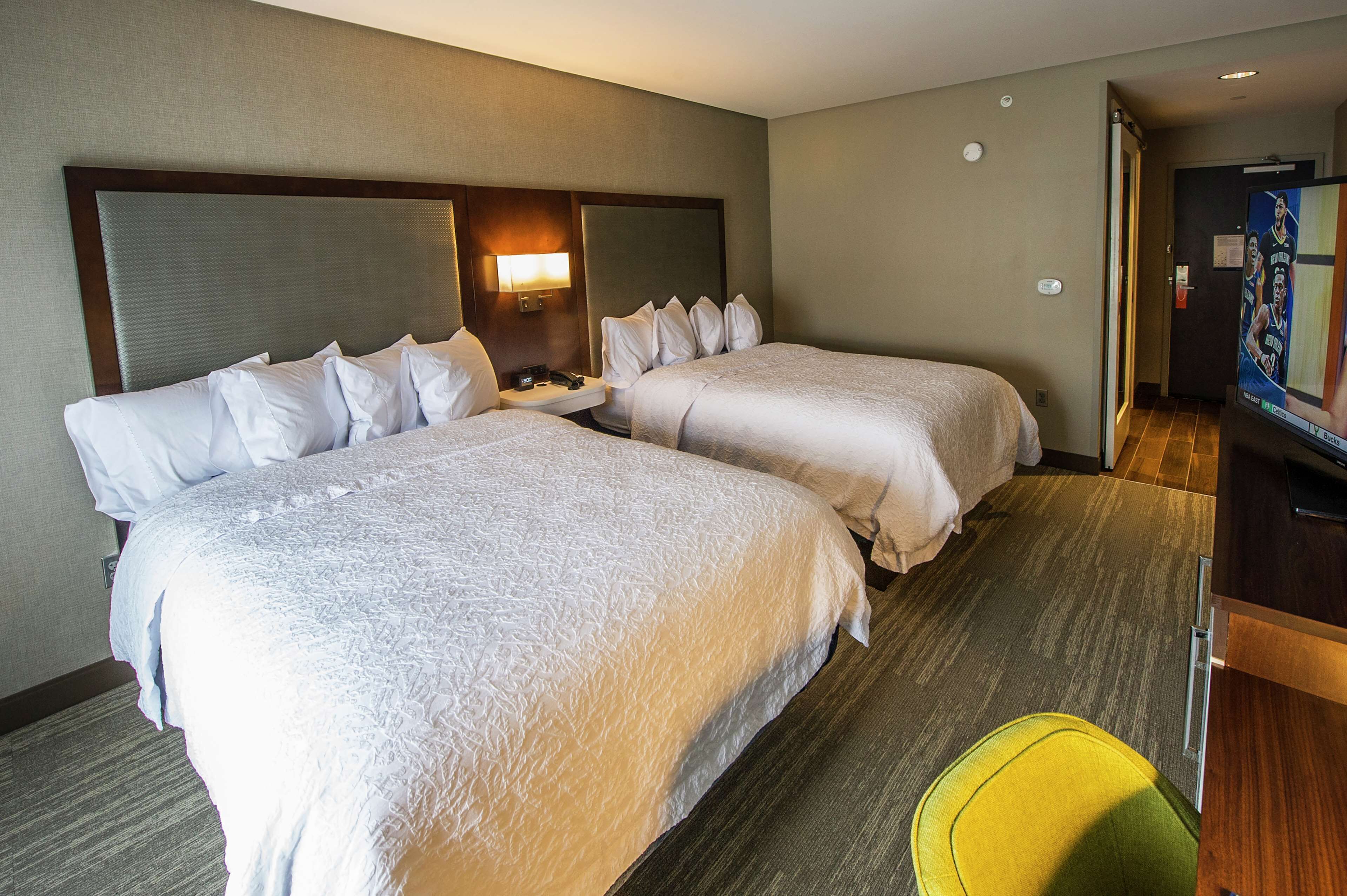 A hotel room with two beds, a bedside table, a lamp, and a television.