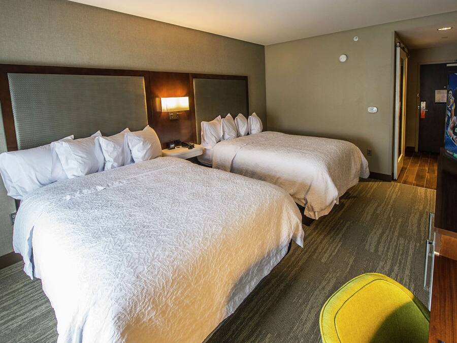 A hotel room with two beds, a bedside table, a lamp, and a television.