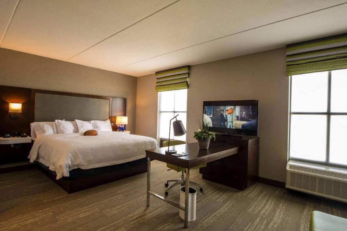 A hotel room with a bed, desk, television, and large windows.