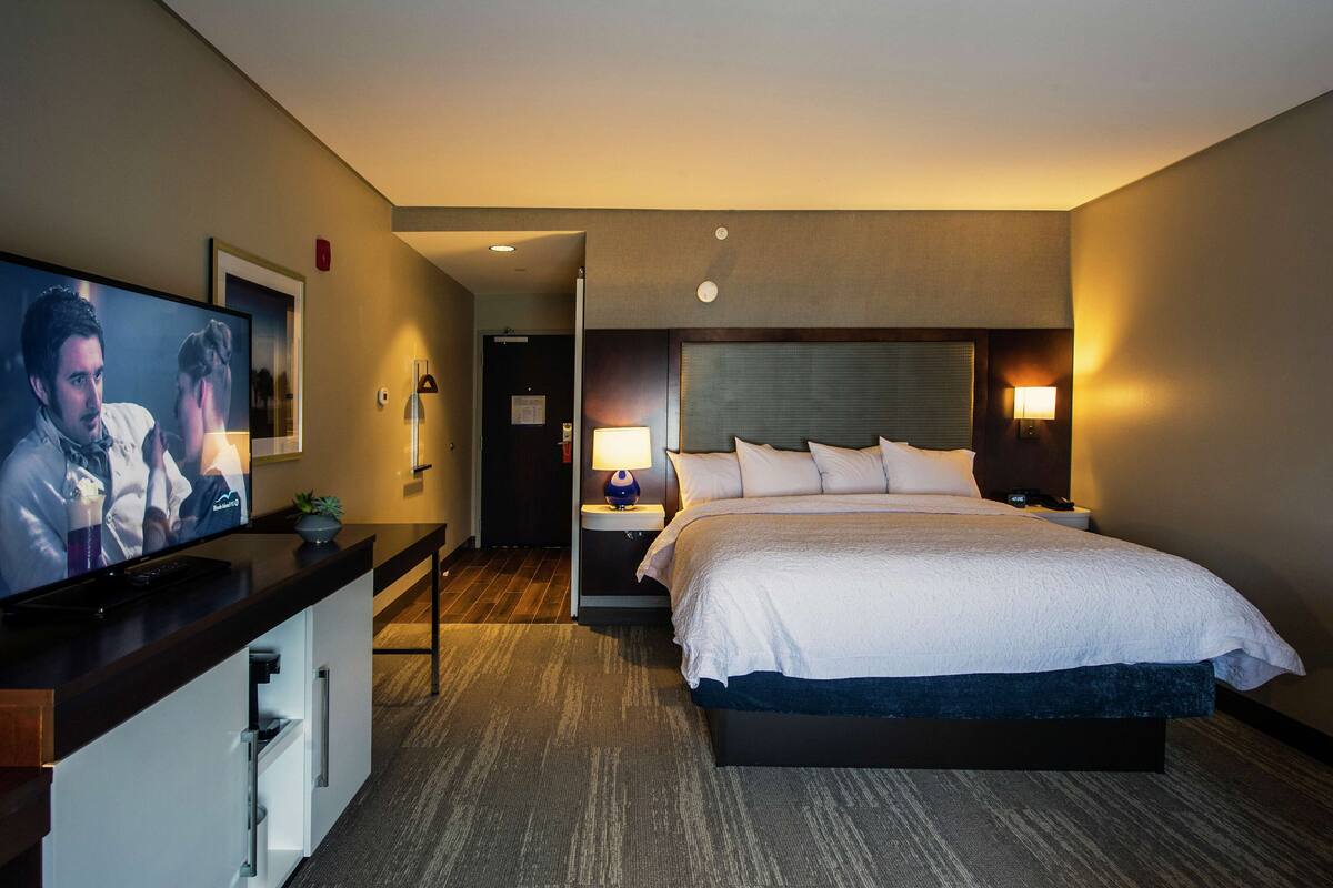 A hotel room with a bed, a TV, a desk, and a nightstand with lamps.