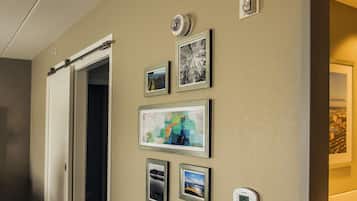 A hallway with a door, a thermostat, and several framed pictures on the wall.