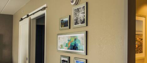 A hallway with a door, a thermostat, and several framed pictures on the wall.