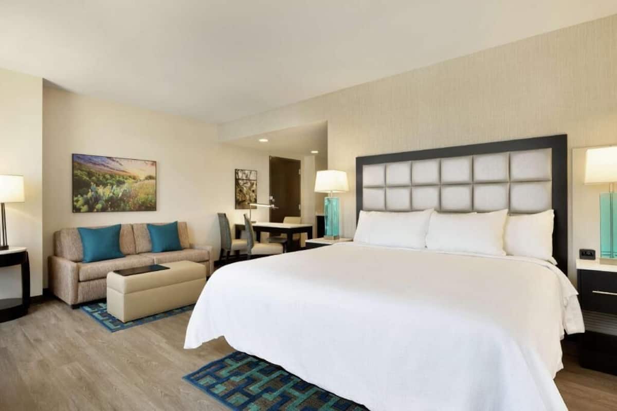 A hotel room with a large bed, a sofa, a desk, and two lamps.