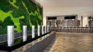 A modern lobby with a green wall, a marble reception desk, and a herringbone floor pattern.