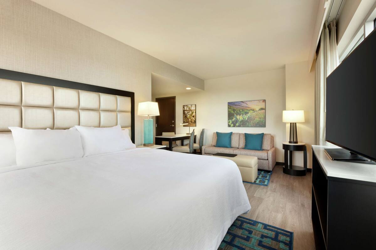 A hotel room with a large bed, a sofa, a TV, and a desk.