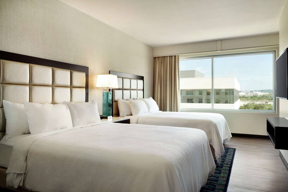 A hotel room with two beds, a large window, and a city view.