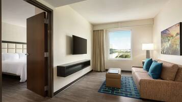 A hotel room with a bed, a sofa, a TV, a window with a view, and a painting on the wall.