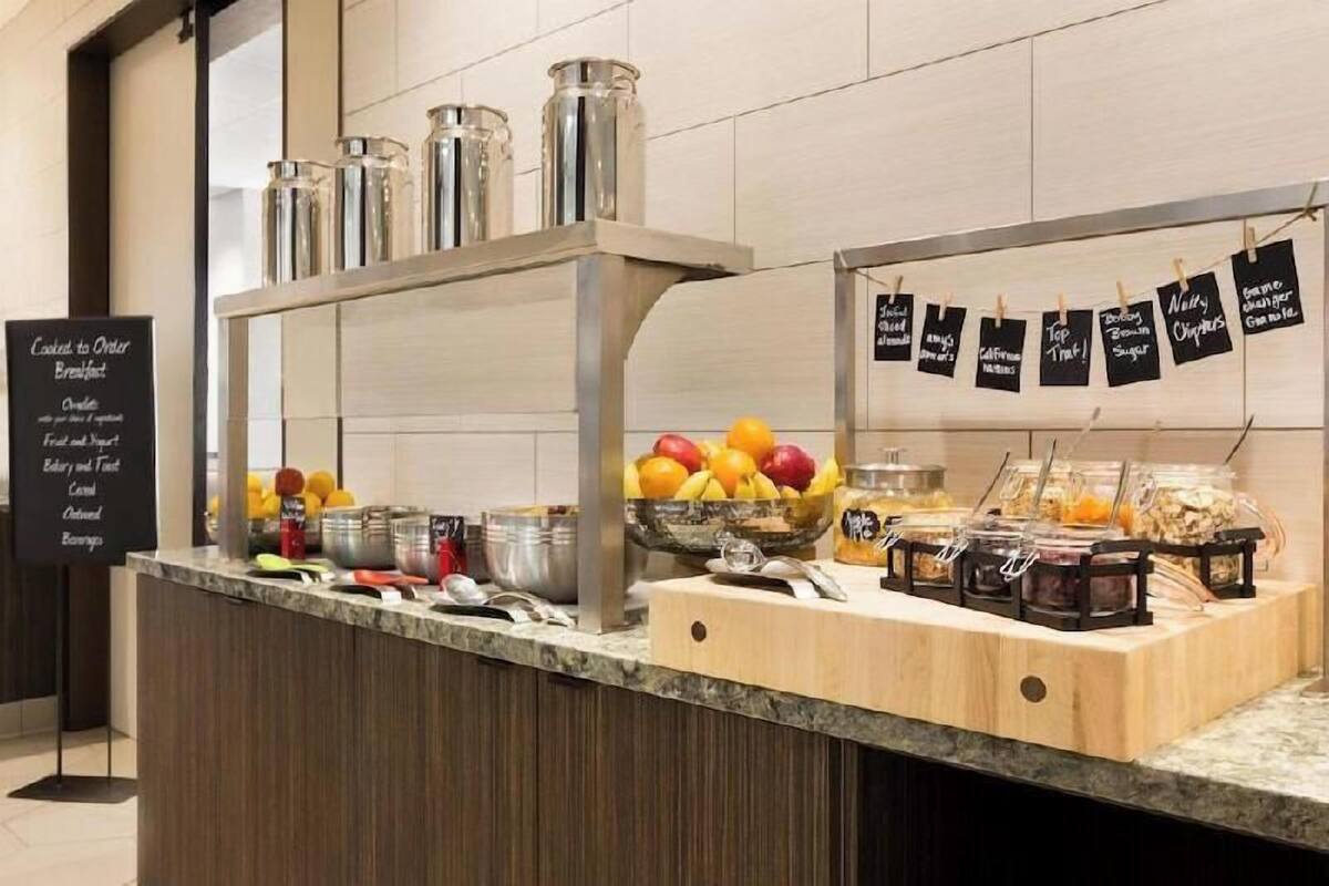 A breakfast bar with a variety of food items, including fruits and condiments, and a sign listing breakfast options.