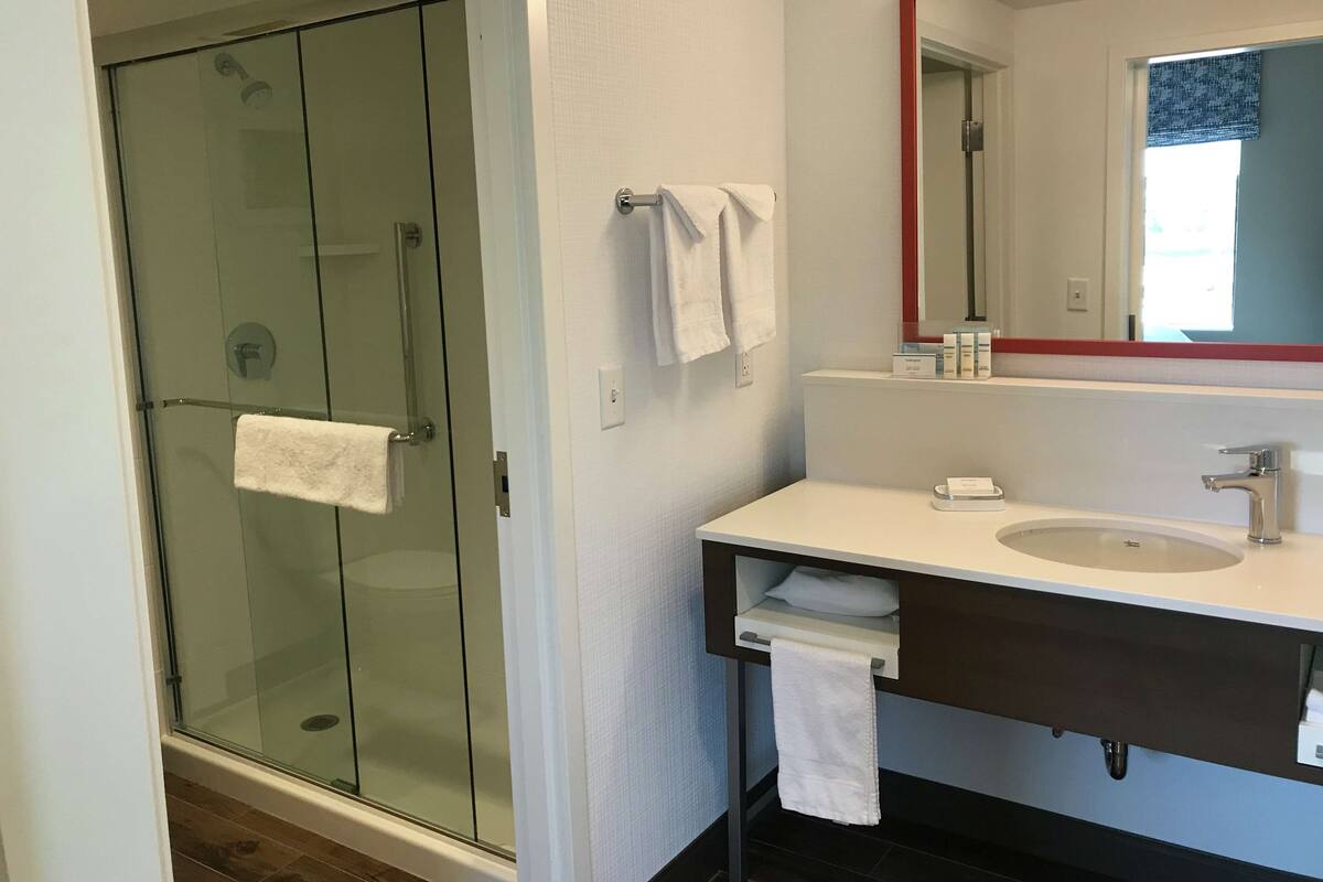 A modern bathroom with a glass shower enclosure, a white sink with a mirror, and a towel rack.