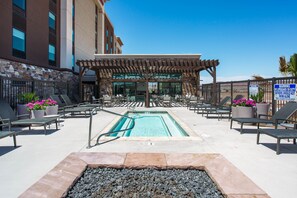A pool area with lounge chairs, a pergola, and a sign warning about diving.
