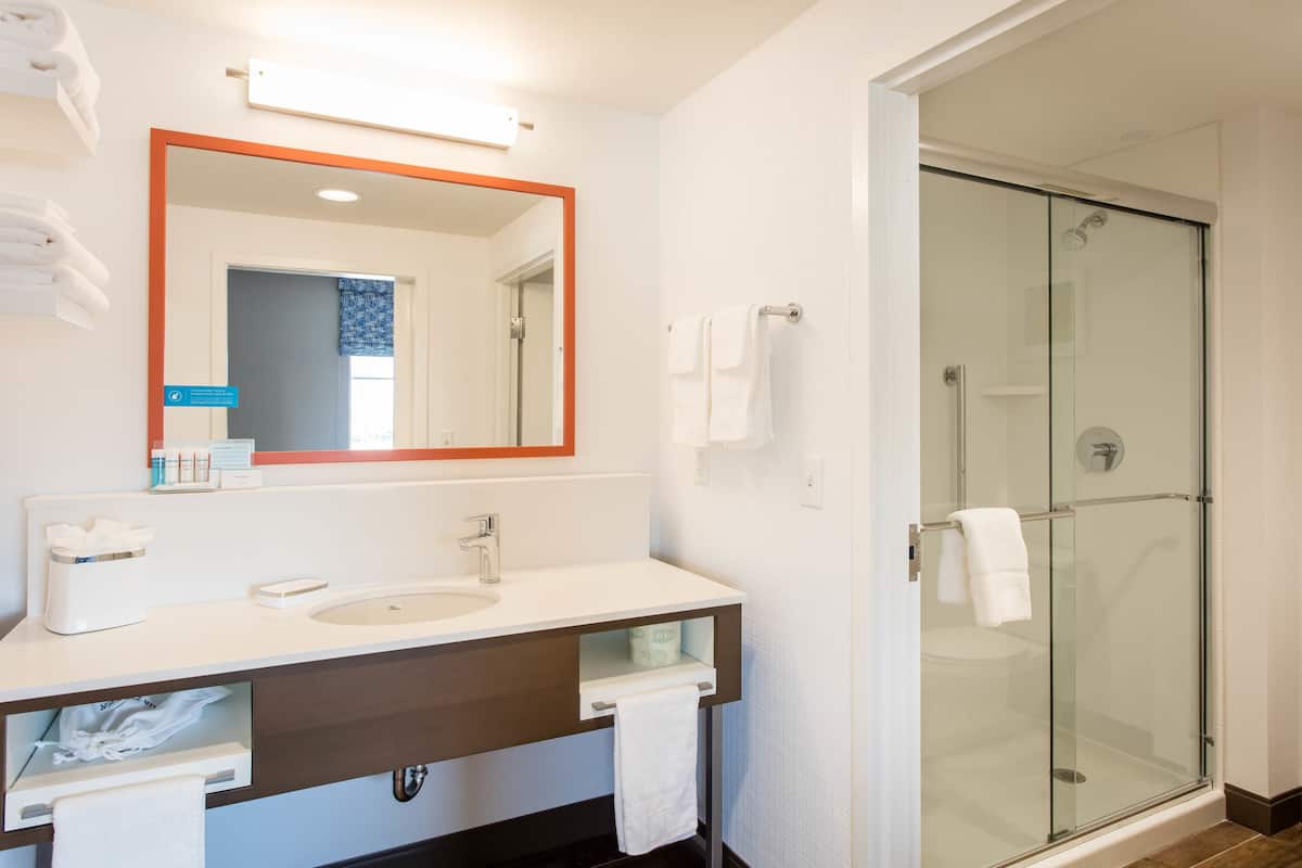 A modern bathroom with a glass shower enclosure, a white sink, and a mirror with a wooden frame.