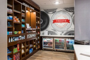 Una sección de aperitivos y dulces con estantes llenos de diferentes opciones, un mural en la pared y dos refrigeradores para bebidas.