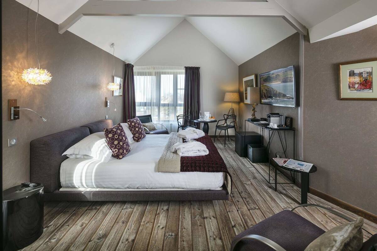 Ein Hotelzimmer mit einem großen Bett, einem Schreibtisch, einem Stuhl, einem Fernseher und einem Fenster mit Vorhängen.