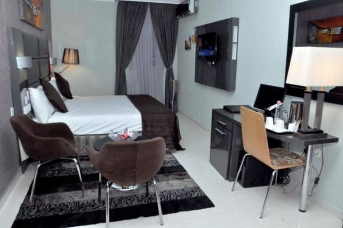 A modern hotel room with a bed, desk, chair, and TV.
