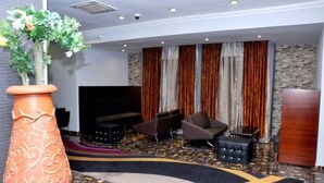 A modern lobby with a curved carpet, a large decorative vase, and a seating area with sofas and a TV. - De Edge Hotel (Port Harcourt)
