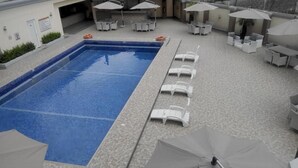 A swimming pool with lounge chairs and umbrellas, surrounded by a tiled patio area. - De Edge Hotel (Port Harcourt)