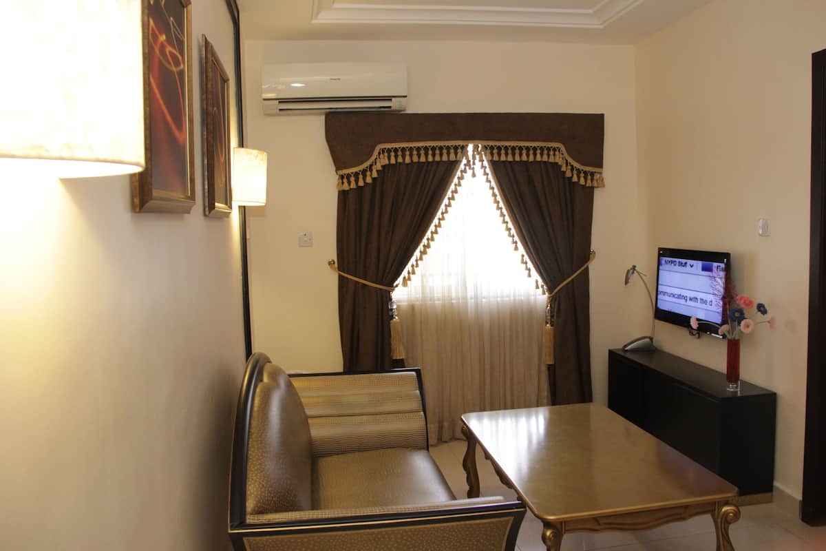 A hotel room with a sofa, a dining table, a TV on a stand, and a window with curtains.
