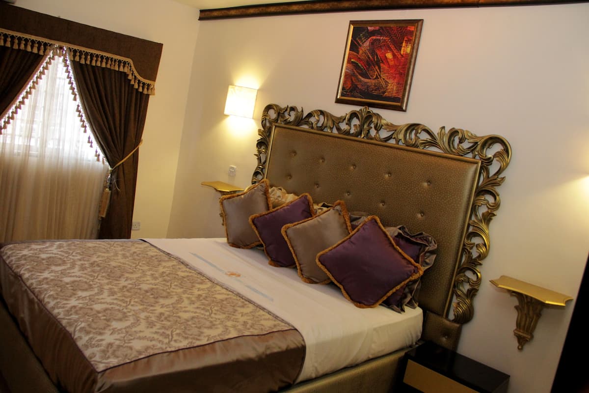 A neatly made bed with a patterned bedspread and decorative pillows, a classic headboard, and a wall-mounted light fixture.