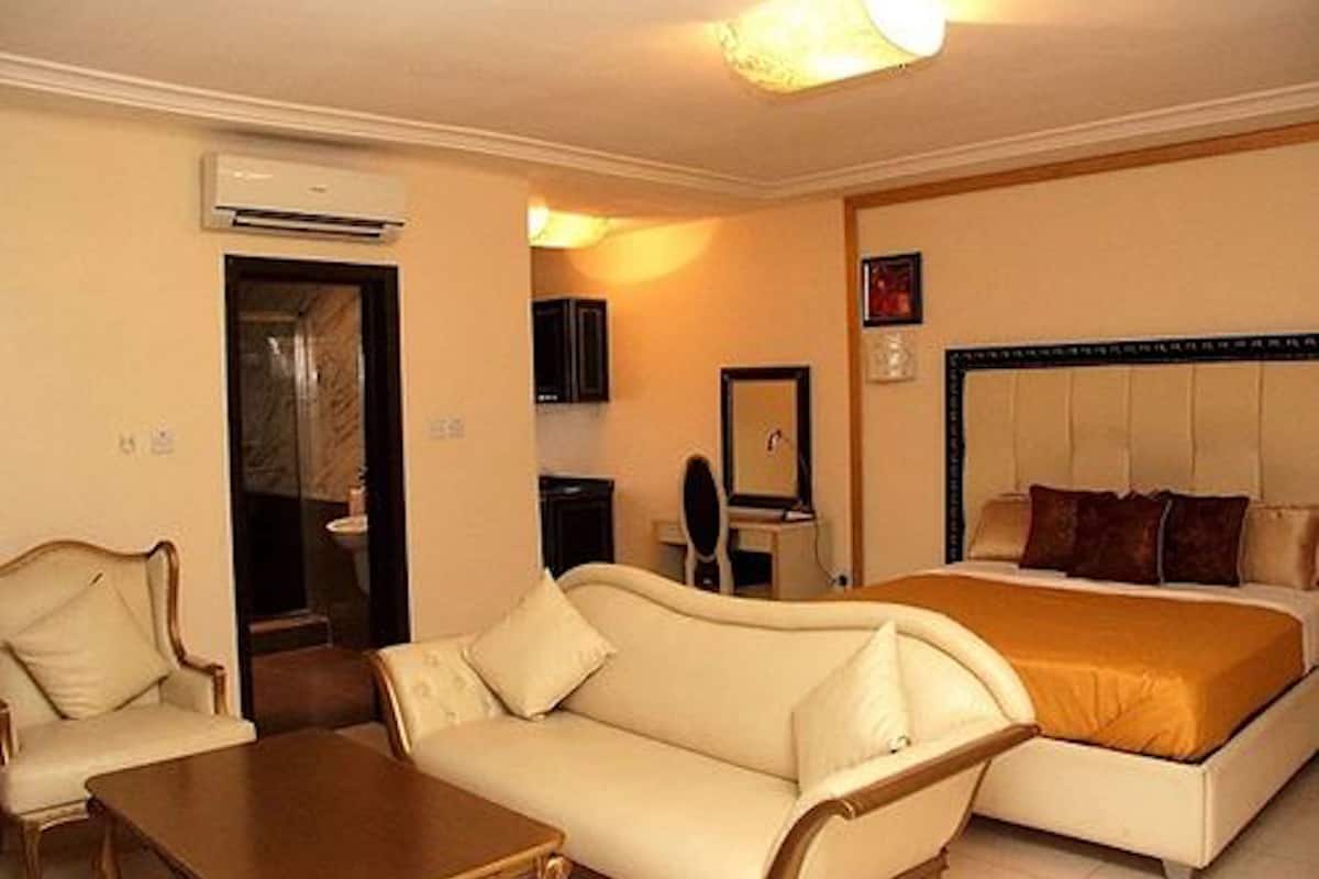A hotel room with a bed, a sofa, a table, and an air conditioning unit.