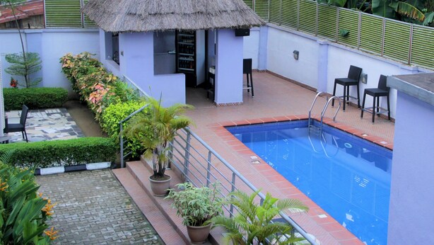 A swimming pool with a thatched-roof structure, potted plants, and outdoor seating. - Calabar Harbour Resort SPA (Calabar)