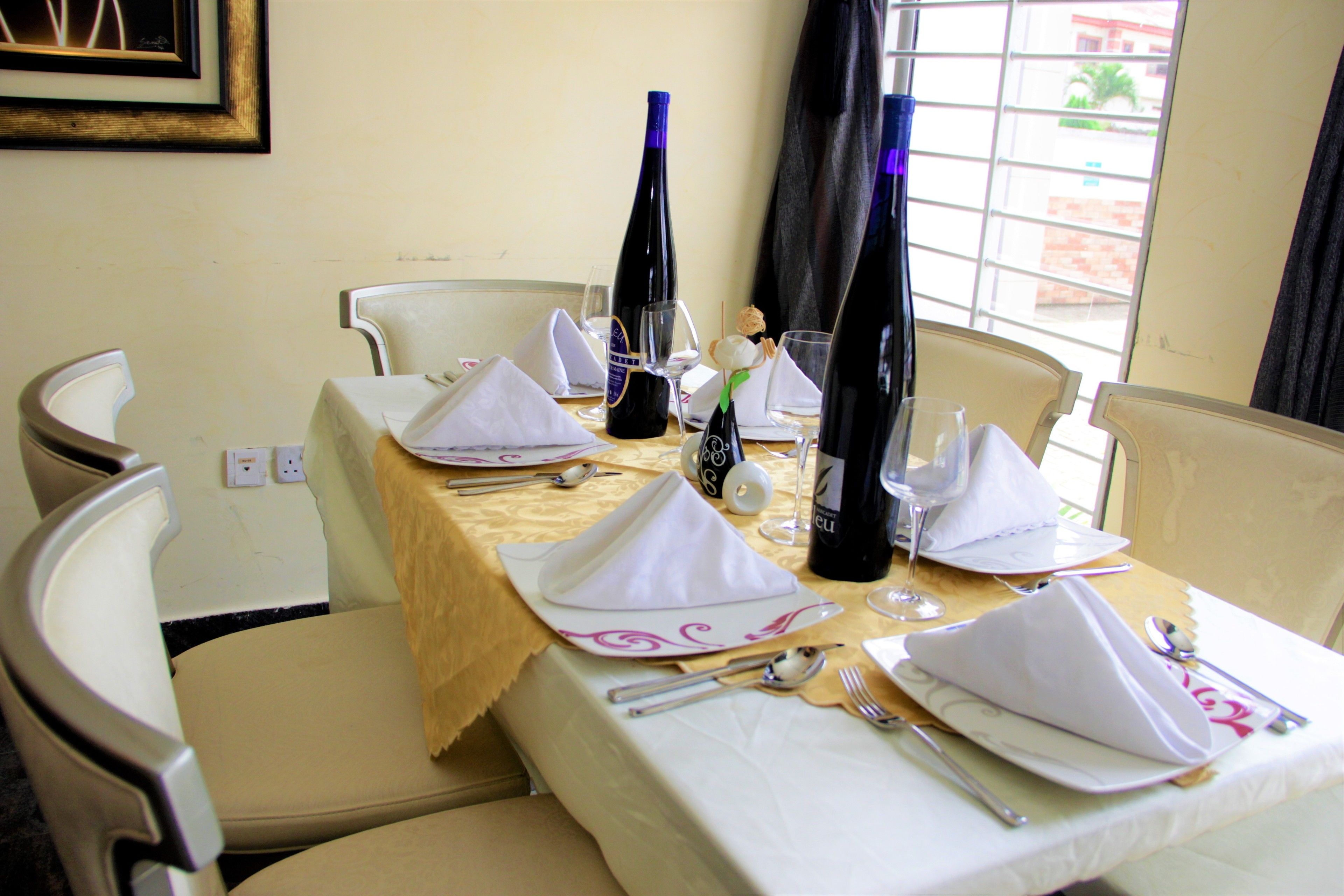 A dining table set with white napkins, silverware, and wine glasses, with a bottle of wine and a small decorative item on the table.