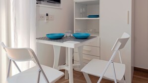 A modern kitchen with white cabinetry, a flat-screen TV, and a dining table with two chairs. - Maison Cipriani (Massa Lubrense)
