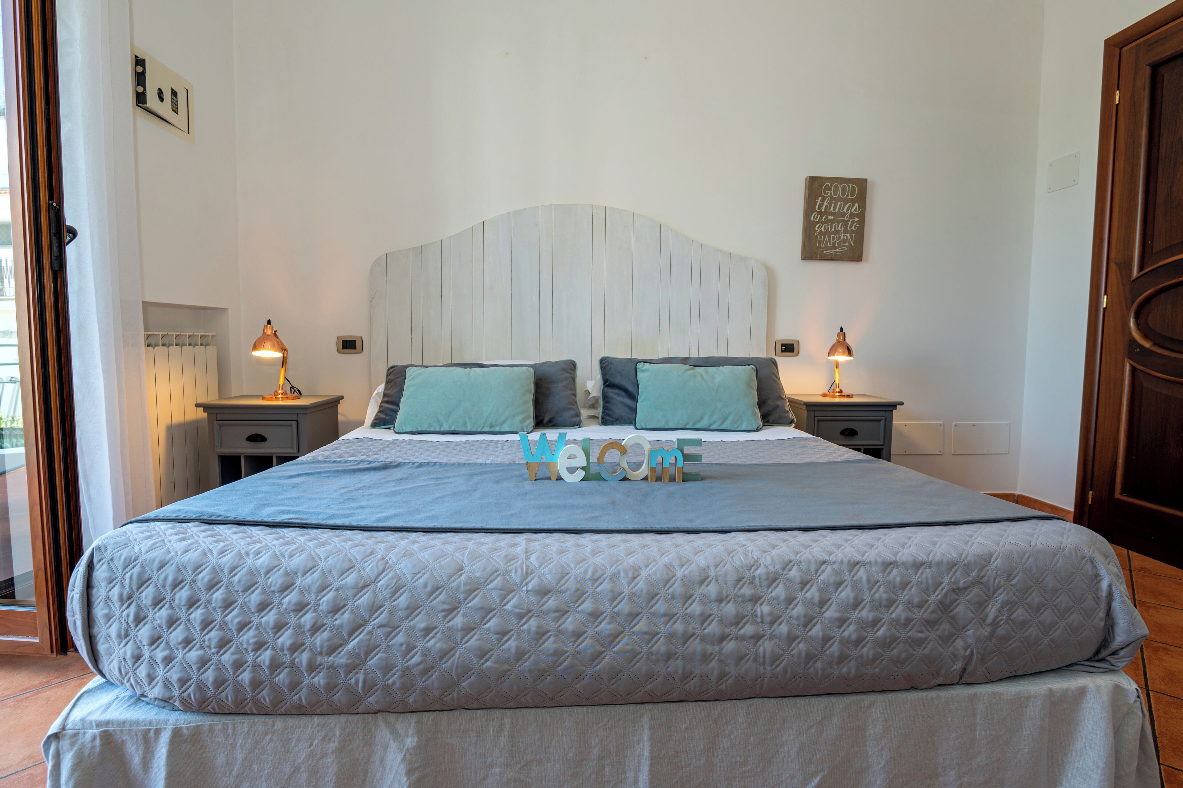 Ein Doppelbett mit gesteppter Bettdecke, zwei Nachttische mit Lampen und ein 'Welcome'-Schild am Bett.