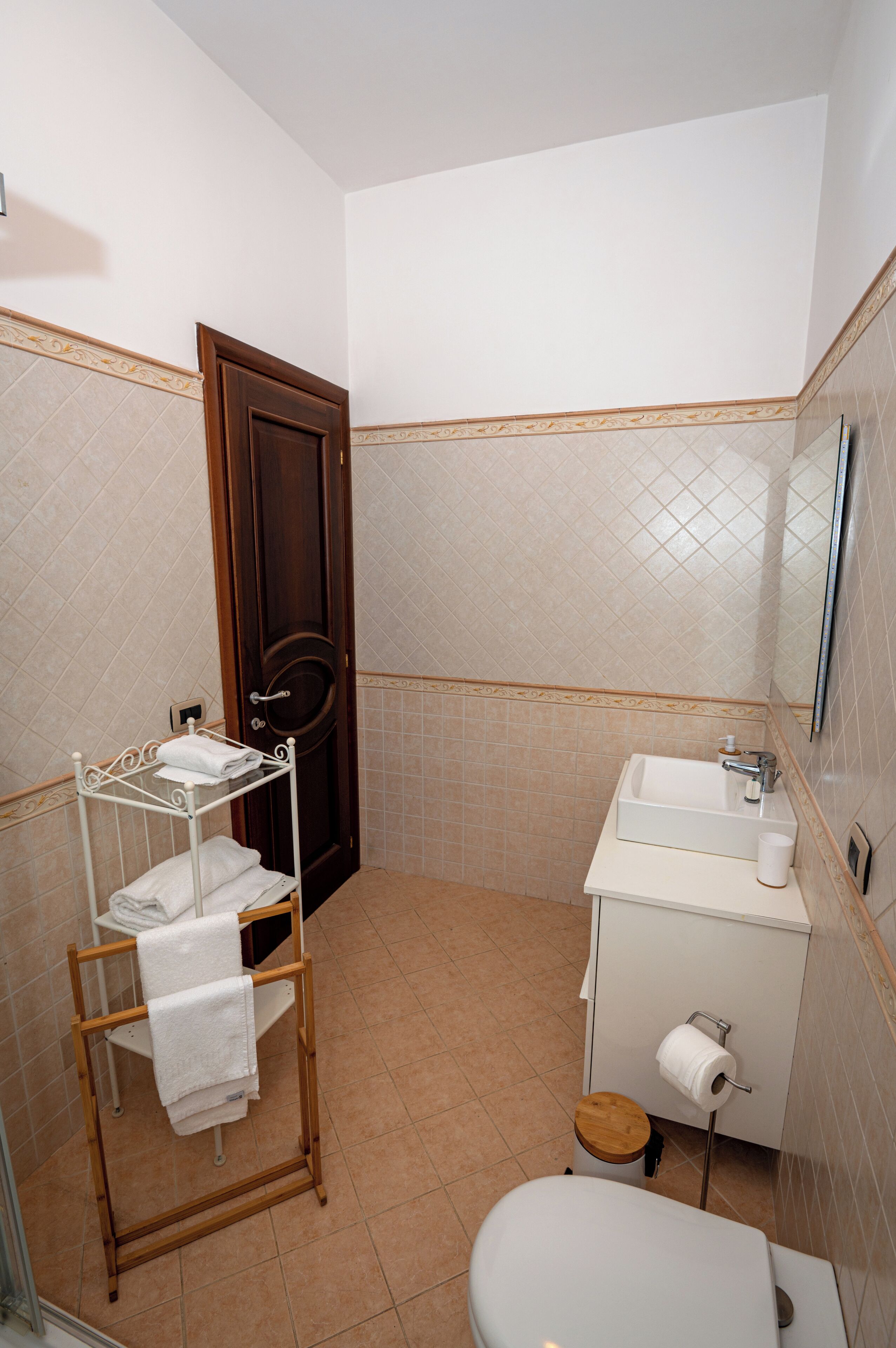Un baño con puerta de madera, un lavabo blanco, un inodoro y un perchero para toallas.