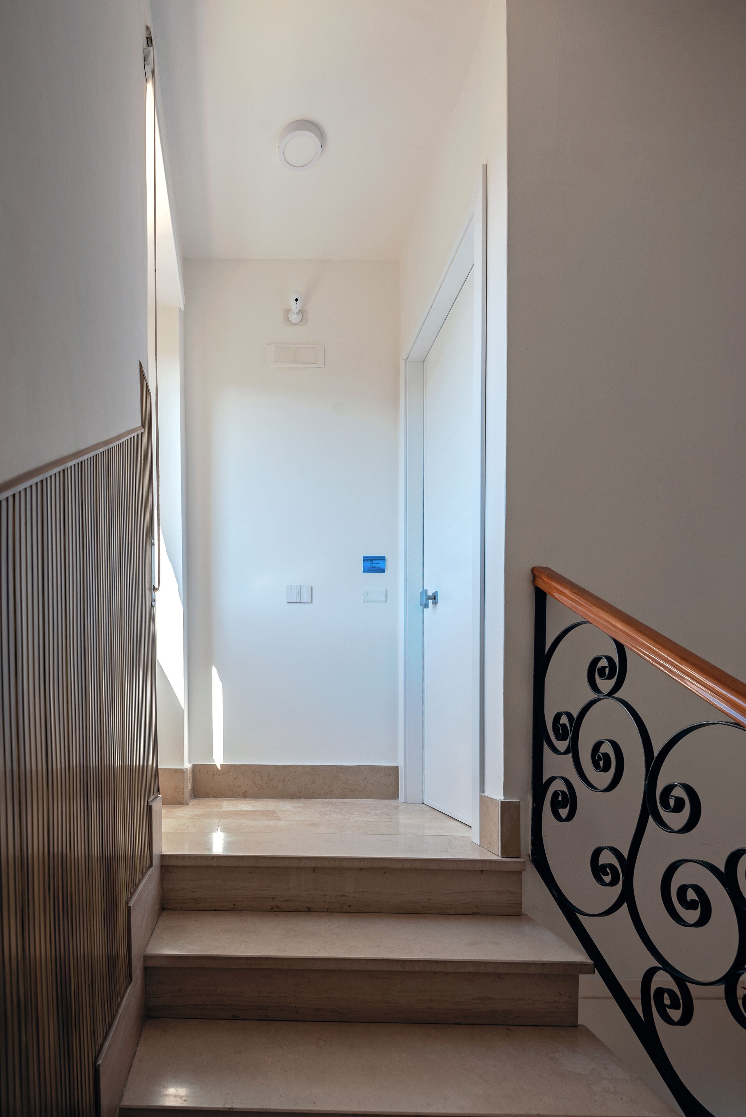 A staircase with a wooden handrail and a metal balustrade, leading to a white door with a blue sign.