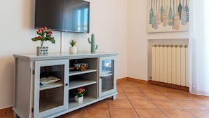 A living room with a TV mounted on the wall, a cabinet with glass doors, and a cactus on top. - Maison Cipriani (Massa Lubrense)