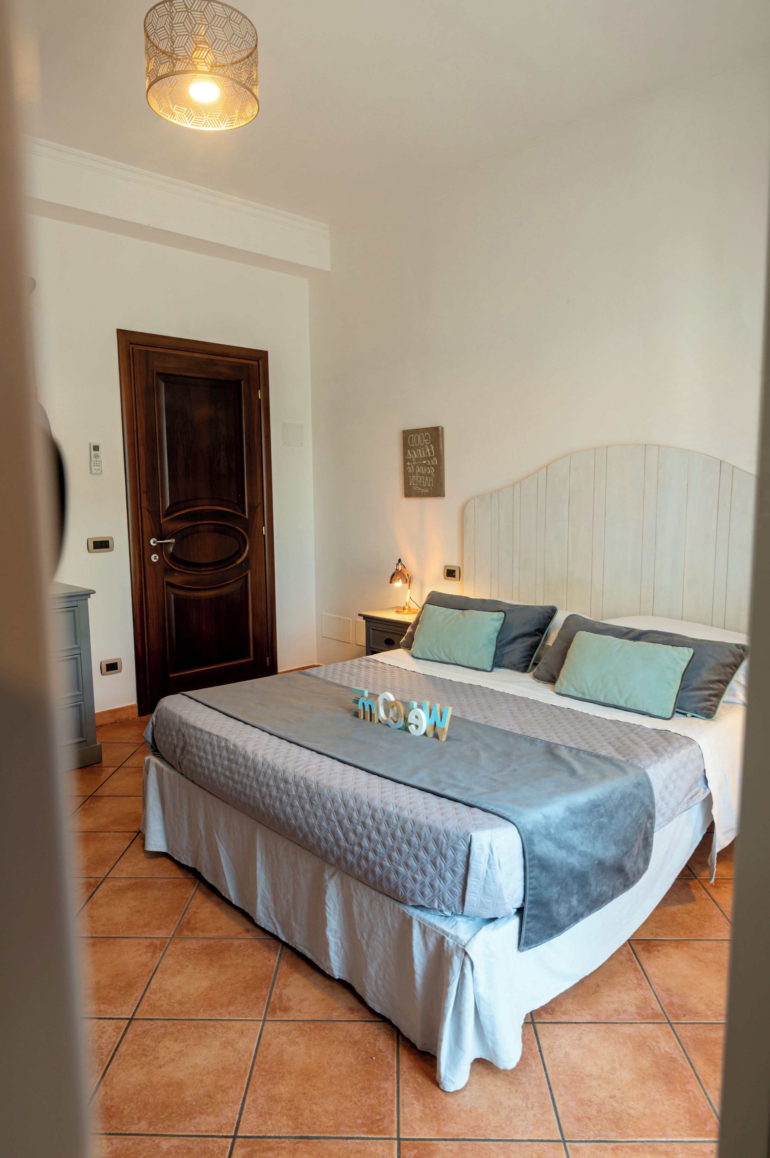 A bedroom with a bed, a nightstand, a wall-mounted lamp, a door, and a ceiling light fixture.