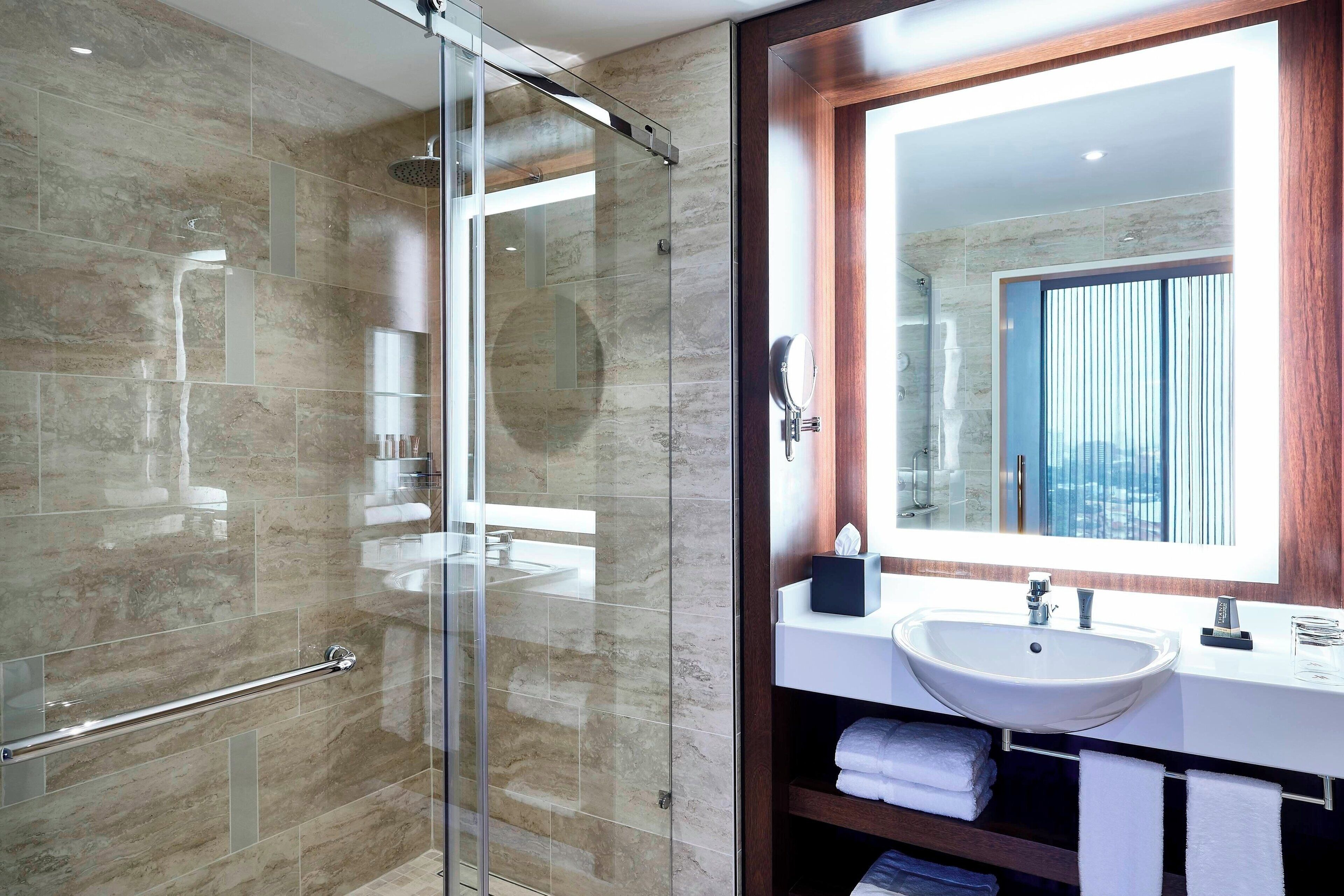 A modern bathroom with a glass-enclosed shower, a large mirror, and a white sink.