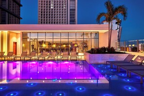 A modern hotel with a rooftop pool featuring illuminated blue and purple lights, lounge chairs, and a palm tree. - Marriott Santa Cruz de la Sierra Hotel (Santa Cruz)