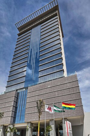 Un hotel alto de diseño moderno, con llamativa fachada vertical de vidrio azul y techo plano con barandilla.