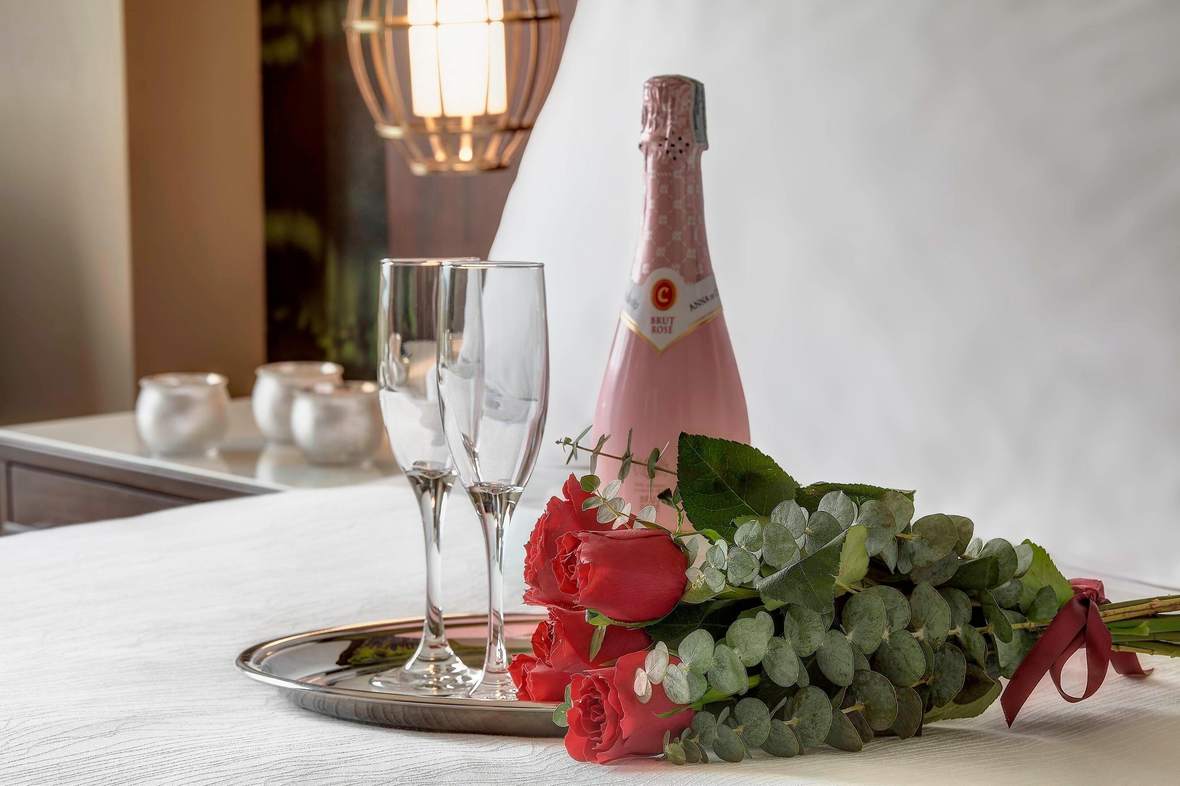 Ein Tisch mit einer Champagnerflasche, zwei Gläsern und einem Strauß roter Rosen.