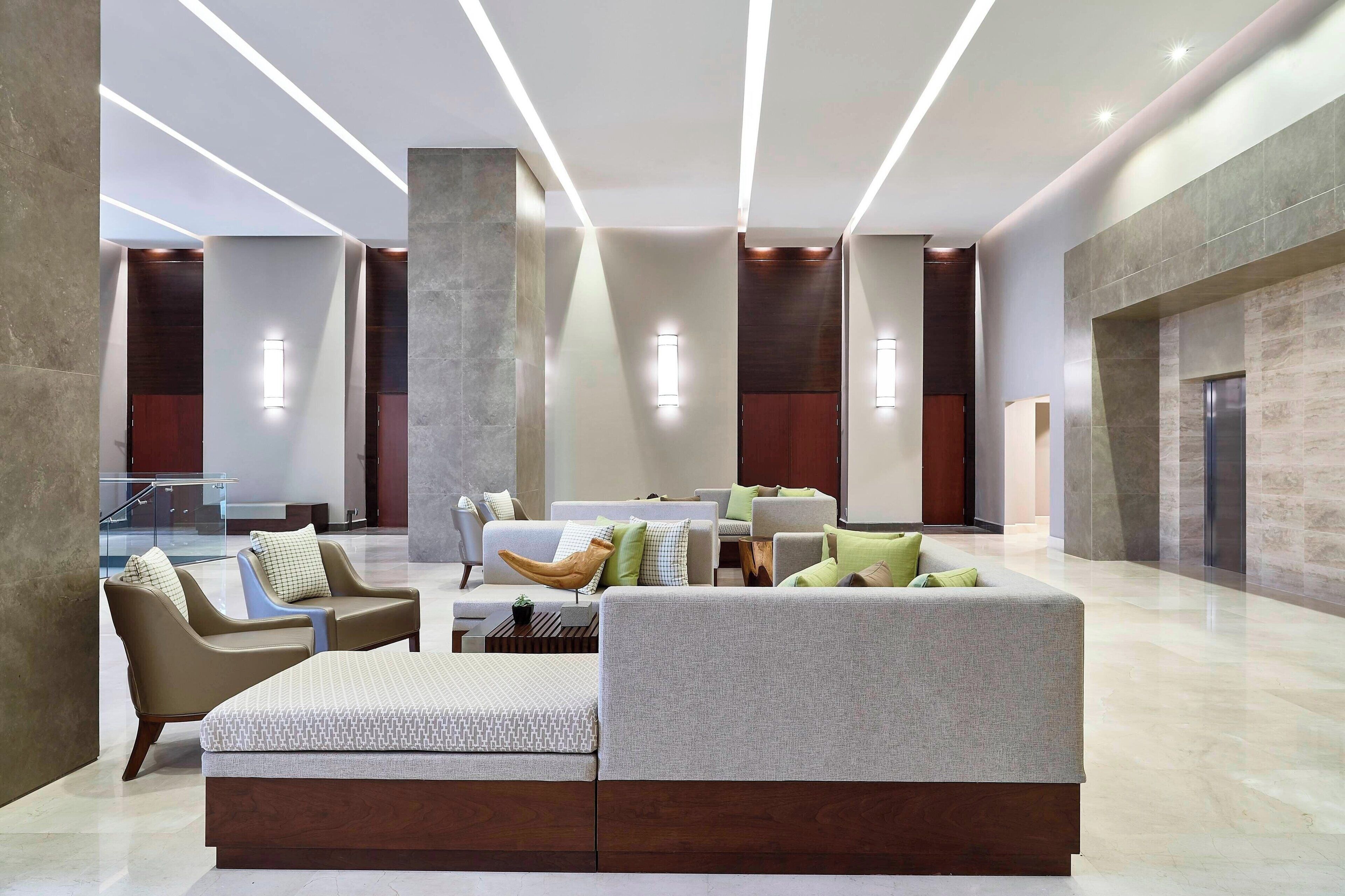 Un hall d’entrée spacieux au design moderne, comprenant un grand espace salon avec des canapés et des fauteuils, une table basse et une petite table d’appoint agrémentée d’une plante.