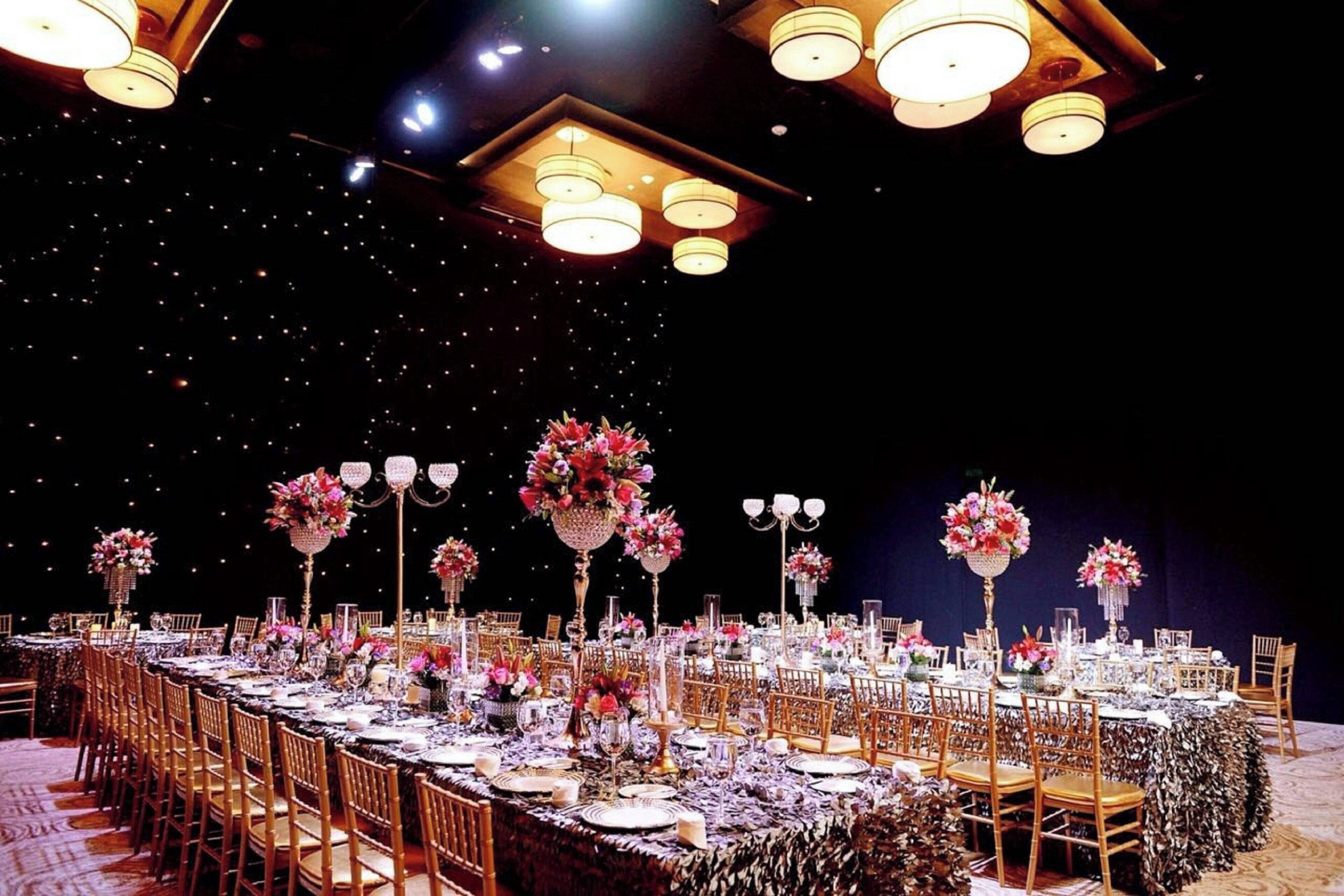 A banquet hall with long tables set for a formal event, adorned with floral centerpieces and candle holders.