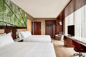 Habitación de hotel con dos camas, un escritorio, un televisor y un ventanal grande con cortinas.