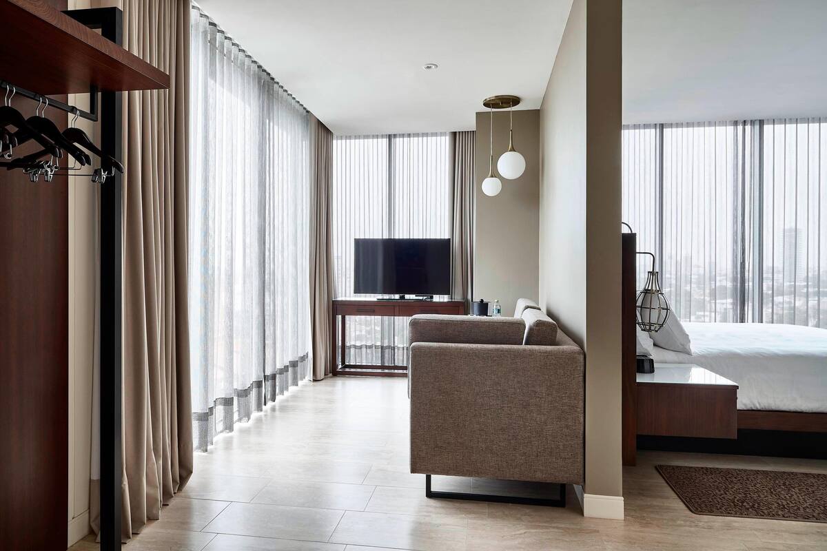 Una habitación de hotel moderna con sofá, cama, televisión y escritorio con computadora.