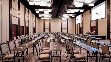 A conference room with multiple tables and chairs, a stage, and a large screen.